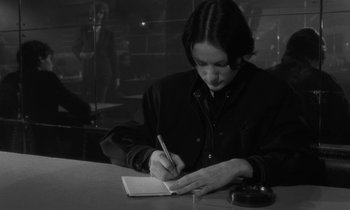 Movie still from “The State of Things” (1982), directed by Wim Wenders – A woman writing on a notepad at a table; Medium shot, Over the shoulder angle