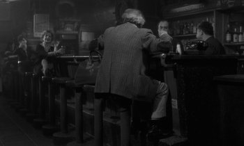 Movie still from “The State of Things” (1982), directed by Wim Wenders – A man sitting at a table in front of two other men; Wide shot, Over the shoulder angle