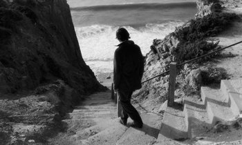 Movie still from “The State of Things” (1982), directed by Wim Wenders – A man walking down a set of stairs near the ocean; Wide shot, High angle