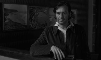 Movie still from “The State of Things” (1982), directed by Wim Wenders – Black and white photograph of a man sitting at a bar; Medium shot, Low angle