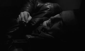 Movie still from “The State of Things” (1982), directed by Wim Wenders – A man laying on the ground holding a cell phone; Close Up shot, High angle