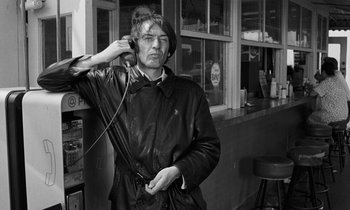 Movie still from “The State of Things” (1982), directed by Wim Wenders – A man in a leather jacket is holding his ear buds; Medium shot, Low angle