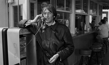 Movie still from “The State of Things” (1982), directed by Wim Wenders – A man talking on a cell phone while wearing a leather jacket; Medium shot, Low angle