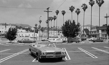Movie still from “The State of Things” (1982), directed by Wim Wenders – An old car parked in a parking lot with palm trees in the background; Extreme Wide shot, High angle
