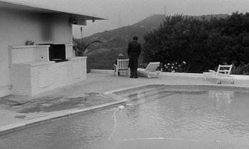 Movie still from “The State of Things” (1982), directed by Wim Wenders – A man standing next to an outdoor swimming pool; Extreme Wide shot, High angle