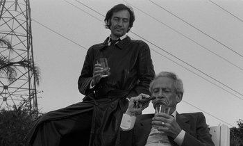 Movie still from “The State of Things” (1982), directed by Wim Wenders – A man and a man smoking a cigarette and drinking a glass of water; Medium shot, Low angle