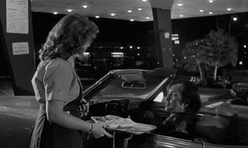 Movie still from “The State of Things” (1982), directed by Wim Wenders – A woman handing a tray of food to a man in the back of a car; Medium shot, Over the shoulder angle