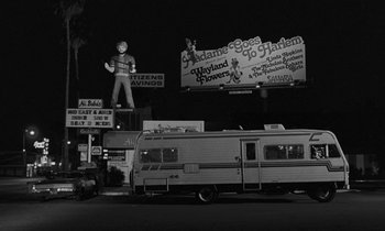 Movie still from “The State of Things” (1982), directed by Wim Wenders – A black - and - white photo of a street sign and a trailer; Wide shot, Low angle