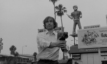 Movie still from “The State of Things” (1982), directed by Wim Wenders – A black and white photo of a man taking a picture; Medium shot, Low angle