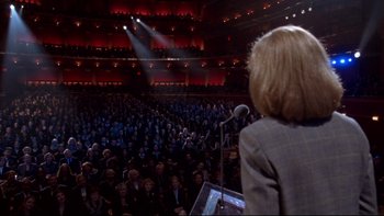 Movie still from “The Stepford Wives” (2004), directed by Frank Oz – A woman standing in front of a microphone in front of an audience; Extreme Wide shot, High angle