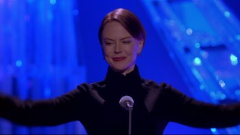 Movie still from “The Stepford Wives” (2004), directed by Frank Oz – A woman standing in front of a microphone on a stage; Medium shot, Low angle