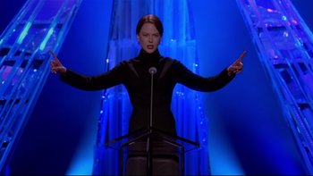 Movie still from “The Stepford Wives” (2004), directed by Frank Oz – A woman standing at a podium in front of a microphone; Medium shot, Low angle