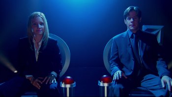 Movie still from “The Stepford Wives” (2004), directed by Frank Oz – A man and a woman sitting in chairs in front of each other in front of a blue background; Medium shot, High angle