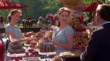 Movie still from “The Stepford Wives” (2004), directed by Frank Oz – A woman standing next to a table full of desserts; Medium shot, Over the shoulder angle