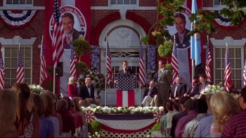 Movie still from “The Stepford Wives” (2004), directed by Frank Oz – A man is giving a speech in front of a crowd of onlookers; Wide shot, High angle