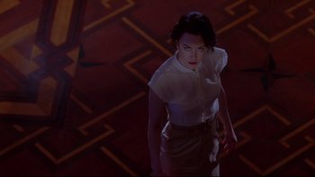 Movie still from “The Stepford Wives” (2004), directed by Frank Oz – A woman in a white shirt and brown skirt standing in a dark room; Wide shot, High angle