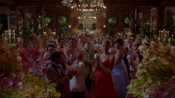 Movie still from “The Stepford Wives” (2004), directed by Frank Oz – A group of people in formal wear clapping in front of a chandelier; Wide shot, Low angle