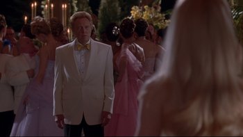 Movie still from “The Stepford Wives” (2004), directed by Frank Oz – A man in a white tuxedo standing in front of a group of people; Medium shot, Over the shoulder angle