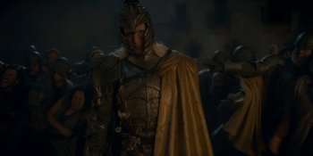 Movie still from “House of the Dragon” (2022), created by George R.R. Martin – A man wearing a helmet and armor standing in front of a group of people; Medium shot, Low angle