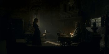 Movie still from “House of the Dragon” (2022), created by George R.R. Martin – A woman and a man sitting at a table in a dimly - lit room; Wide shot, Low angle