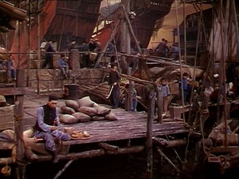 Movie still from “The Story of Dr. Wassell” (1944), directed by Cecil B. DeMille – A man sitting on top of a wooden dock; Wide shot, High angle