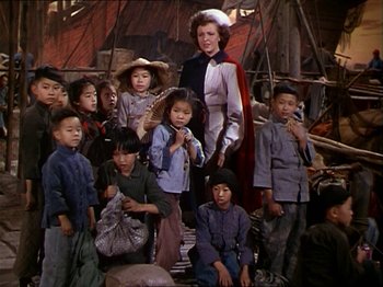 Movie still from “The Story of Dr. Wassell” (1944), directed by Cecil B. DeMille – A group of children sitting around a woman; Medium shot, High angle