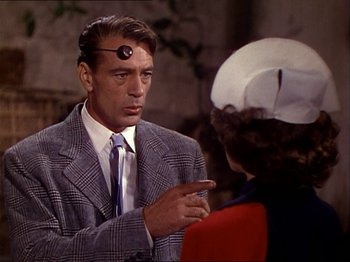Movie still from “The Story of Dr. Wassell” (1944), directed by Cecil B. DeMille – An older man wearing a suit and tie talking to an older woman wearing a hat; Close Up shot, Over the shoulder angle