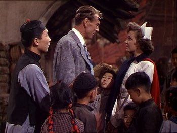 Movie still from “The Story of Dr. Wassell” (1944), directed by Cecil B. DeMille – A group of people standing around each other in front of a building; Medium shot, Over the shoulder angle