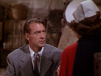 Movie still from “The Story of Dr. Wassell” (1944), directed by Cecil B. DeMille – An older man wearing a suit talking to an older woman wearing a hat; Medium shot, Over the shoulder angle