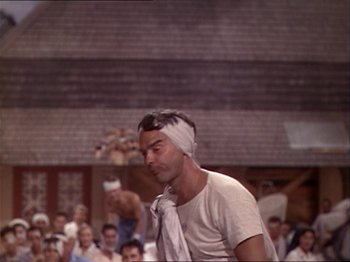 Movie still from “The Story of Dr. Wassell” (1944), directed by Cecil B. DeMille – A man with bandages on his head is standing in front of a group of people; Close Up shot, Low angle