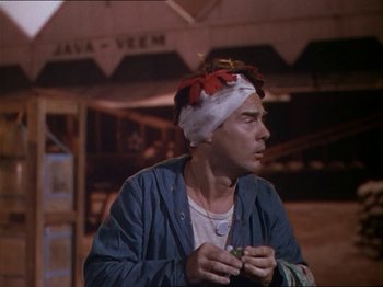Movie still from “The Story of Dr. Wassell” (1944), directed by Cecil B. DeMille – A man with a bandanna on his head is holding something in his hands; Medium shot, Over the shoulder angle