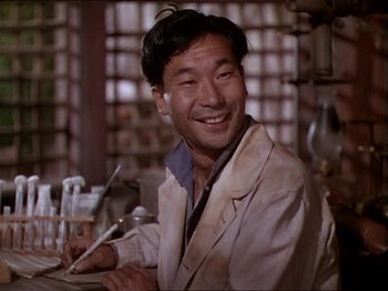 Movie still from “The Story of Dr. Wassell” (1944), directed by Cecil B. DeMille – A man smiles while writing on a piece of paper; Medium shot, Low angle