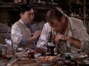 Movie still from “The Story of Dr. Wassell” (1944), directed by Cecil B. DeMille – Two men in lab coats looking at a microscope; Medium shot, Over the shoulder angle