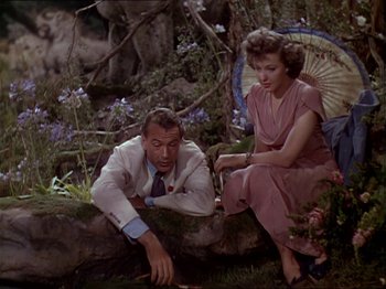 Movie still from “The Story of Dr. Wassell” (1944), directed by Cecil B. DeMille – A man and a woman sitting on the ground in a forest; Medium shot, High angle