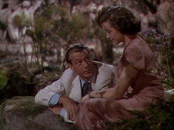 Movie still from “The Story of Dr. Wassell” (1944), directed by Cecil B. DeMille – A man and a woman sitting on the ground in front of trees; Medium shot, High angle