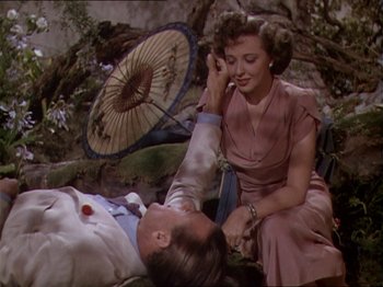 Movie still from “The Story of Dr. Wassell” (1944), directed by Cecil B. DeMille – A man and a woman sitting next to each other on the ground; Medium shot, Overhead angle