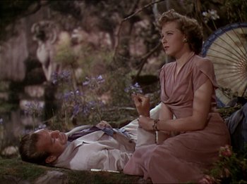 Movie still from “The Story of Dr. Wassell” (1944), directed by Cecil B. DeMille – A man and a woman sitting on the ground in a forest; Medium shot, Overhead angle