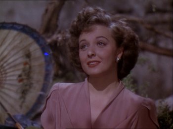 Movie still from “The Story of Dr. Wassell” (1944), directed by Cecil B. DeMille – A woman in a pink dress is smiling for the camera; Close Up shot, Over the shoulder angle