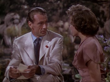 Movie still from “The Story of Dr. Wassell” (1944), directed by Cecil B. DeMille – An older man in a white suit talking to a woman in a pink dress; Medium shot, Over the shoulder angle