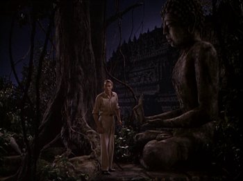 Movie still from “The Story of Dr. Wassell” (1944), directed by Cecil B. DeMille – A man standing in front of a buddha statue in the dark; Wide shot, Low angle