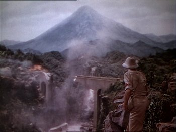 Movie still from “The Story of Dr. Wassell” (1944), directed by Cecil B. DeMille – A man standing in front of a mountain with smoke coming out of it; Wide shot, Over the shoulder angle