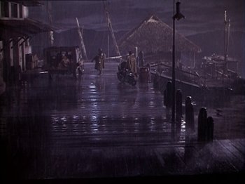 Movie still from “The Story of Dr. Wassell” (1944), directed by Cecil B. DeMille – A group of people on a dock in the rain at night; Extreme Wide shot, High angle