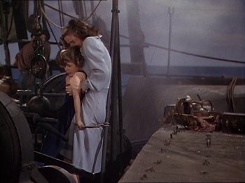 Movie still from “The Story of Dr. Wassell” (1944), directed by Cecil B. DeMille – A woman holding a child in her arms while standing next to a boat; Wide shot, High angle