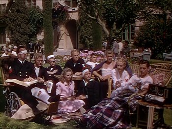 Movie still from “The Story of Dr. Wassell” (1944), directed by Cecil B. DeMille – A group of people sitting on a bench in front of a building; Wide shot, High angle