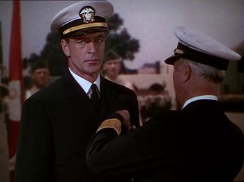 Movie still from “The Story of Dr. Wassell” (1944), directed by Cecil B. DeMille – A man in a naval uniform is being pinned by another man; Medium shot, Over the shoulder angle