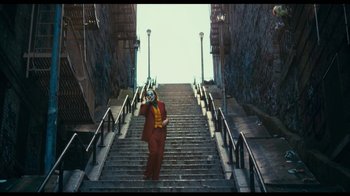 Movie still from “The Story of Film: A New Generation” (2021), directed by Mark Cousins – A man in a suit and mask standing on some stairs; Wide shot, Low angle