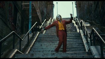 Movie still from “The Story of Film: A New Generation” (2021), directed by Mark Cousins – A man dressed as the joker walks down a set of stairs; Wide shot, Low angle