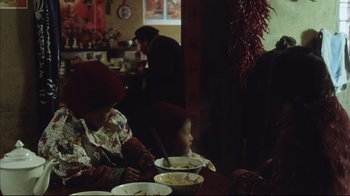 Movie still from “The Story of Qiu Ju” (1992), directed by Yimou Zhang – A woman and a child are sitting at a table eating food; Medium shot, High angle