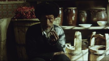 Movie still from “The Story of Qiu Ju” (1992), directed by Yimou Zhang – An old man smoking a cigarette while sitting on a chair; Medium shot, Low angle