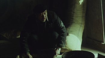 Movie still from “The Story of Qiu Ju” (1992), directed by Yimou Zhang – A man kneeling on the ground in a dark room; Medium shot, High angle
